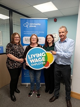 Four people standing in front of a popup stand in an office. They are holding the Living Wage Employer sign.