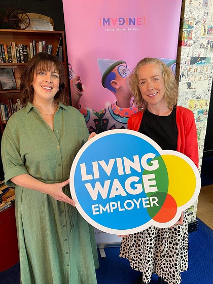 Two people holding the Living Wage Employer sign and smiling at the camera.