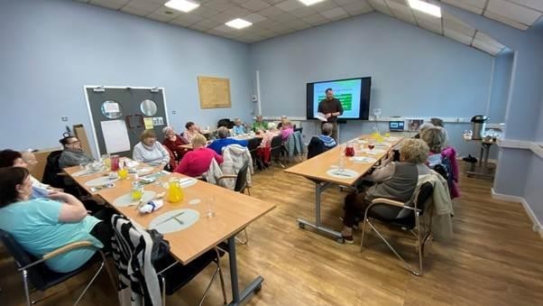 Older people sitting around tables listening to a presentation.