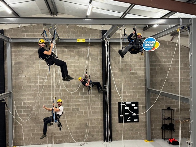 A group of people suspended from ropes, practicing climbing techniques indoors.