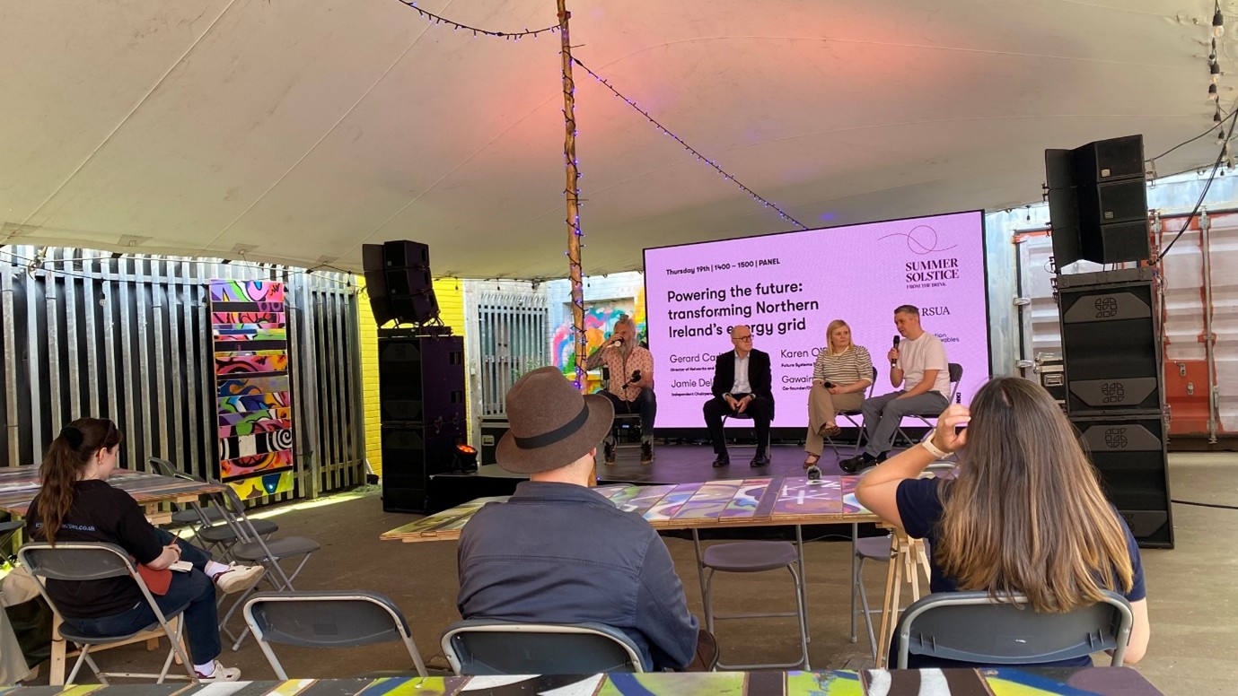 A panel of four people sitting in front of a screen talking to an audience.