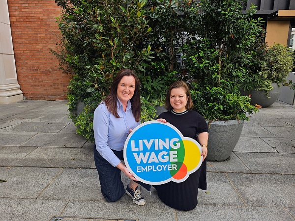 Two people kneeling down in front of green plants and holding a Living Wage Employer sign.
