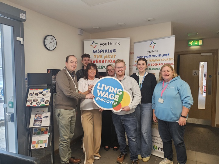 Seven people are standing in an office in front of two pop-up stands. They are looking at the camera and smiling.
