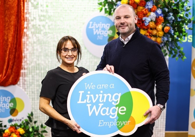 Two people standing in front of a sign that reads "We are a Living Wage Employer".