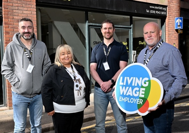 Four people standing outside the Start360 office. One person is holding a sign that reads "Living Wage Employer".